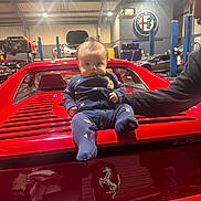 Lando joined the competition — help win amazing prizes! baby, child, car, ferrari, red, garage, luxury_car, automobile, person, man, indoor, lighting, clothing, logo, vehicle, adult, supporting_arm, star_pattern, infant, transportation