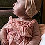 baby, child, chubby_cheeks, couch, curious, cute, furniture, hand, headband, headwear, indoor, infant, pink_clothing, portrait, romper, side_profile, sitting, skin, soft_light, toddler