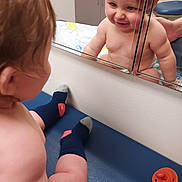 Preston is registered to the contest to win money with this photo: baby, infant, child, mirror, reflection, smiling, happy, indoor, portrait, tummy_time, diaper, bare_chest, sock, pacifier, changing_table, nursery, playful, face, person, home