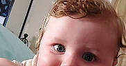 Preston is registered to the contest to win money with this photo: baby, child, infant, portrait, face, eyes, smiling, curly_hair, messy_hair, indoors, bedroom, blanket, blue_blanket, striped_clothing, lying_down, close_up, camera, photograph, home, cute