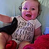 baby, infant, child, smiling, happy, portrait, face, sitting, couch, blanket, clothing, shirt, text_on_clothing, indoor, home, furniture, brown_hair, blue_eyes, cozy, photography