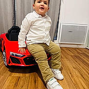 Luis Felipe participe au concours pour gagner de l'argent avec cette photo : toddler, child, white_shirt, beige_pants, white_shoes, toy_car, red_car, indoor, wooden_floor, curtains, smiling, casual_pose, happy, floor, childrens_toy, person, young_child, playtime, home, cute