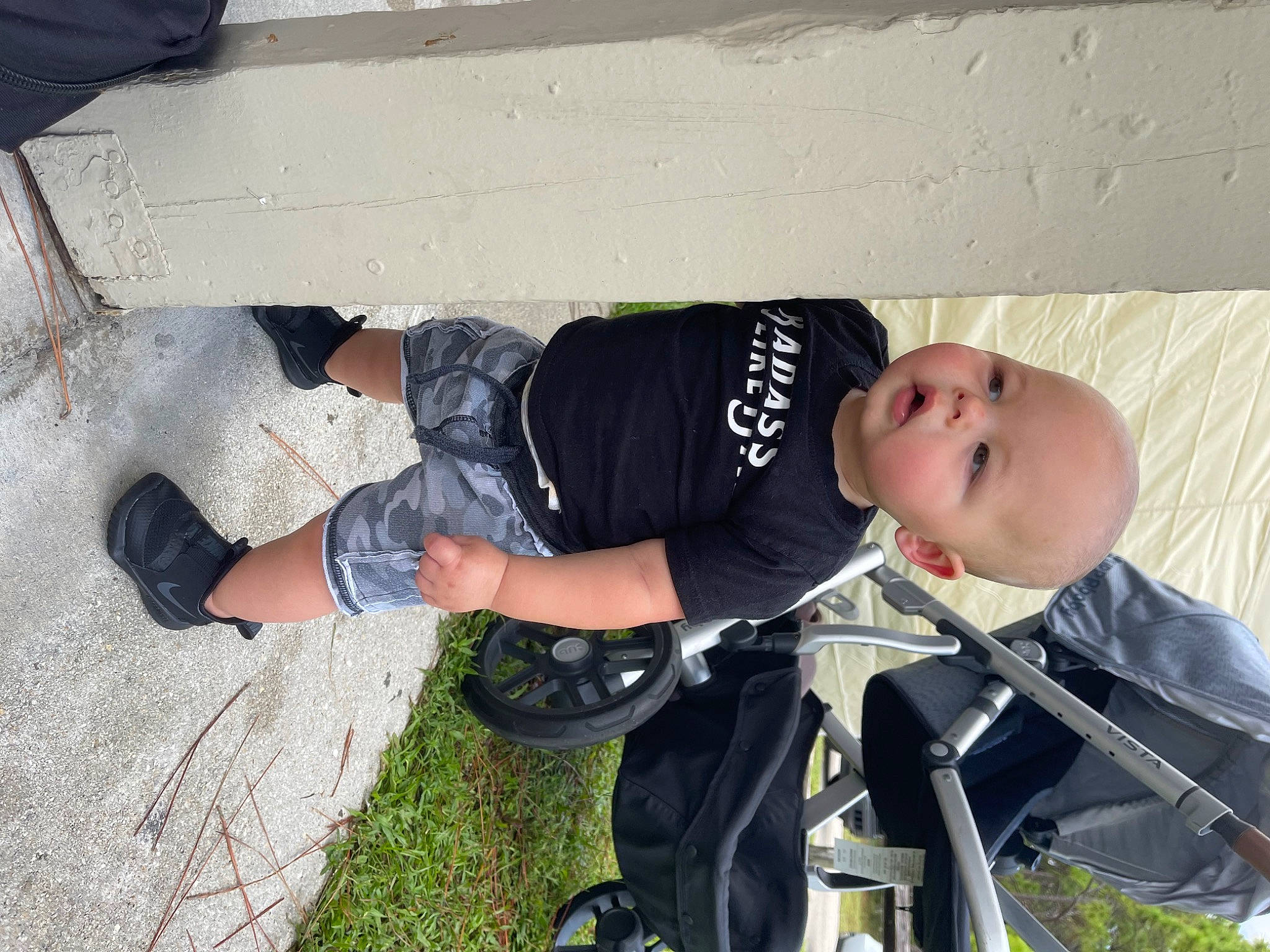 Hudson is registered to the contest to win money with this photo: auto_part, baby, baby_carriage, baby_products, baby_safety, baby_toddler_clothing, child, concrete, fun, grass, human_leg, outdoor_shoe, person, plant, recreation, sandal, sitting, smile, toddler, walking_shoe
