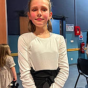 Lyliana a rejoint le concours — aidez-le/la à gagner de superbes lots ! background, black_waist_tie, blue_wall, casual_clothing, chair, child, confident, face, fire_extinguisher, girl, holding, indoor, long_hair, person, smile, standing, toy, white_top, wood_panel, young