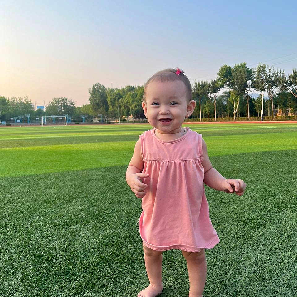 Patricia is registered to the contest to win money with this photo: barefoot, child, cute, daylight, field, grass, grass_texture, happy, nature, outdoor, person, pink_dress, playing, portrait, smiling, sports_field, sunset, toddler, trees, young_child
