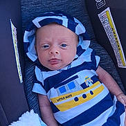 Eric is registered to the contest to win money with this photo: baby, infant, child, portrait, car_seat, indoors, vehicle, sailor_outfit, striped_clothing, blue_clothing, yellow_clothing, hat, tongue_out, wide_eyes, sitting, blanket, cozy, close_up, face, safe