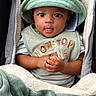 baby, infant, hat, bucket_hat, bib, blanket, cozy, cute, clothing, child, face, hands, portrait, expression, indoor, soft_texture, striped_shirt, seated, warm, adorable