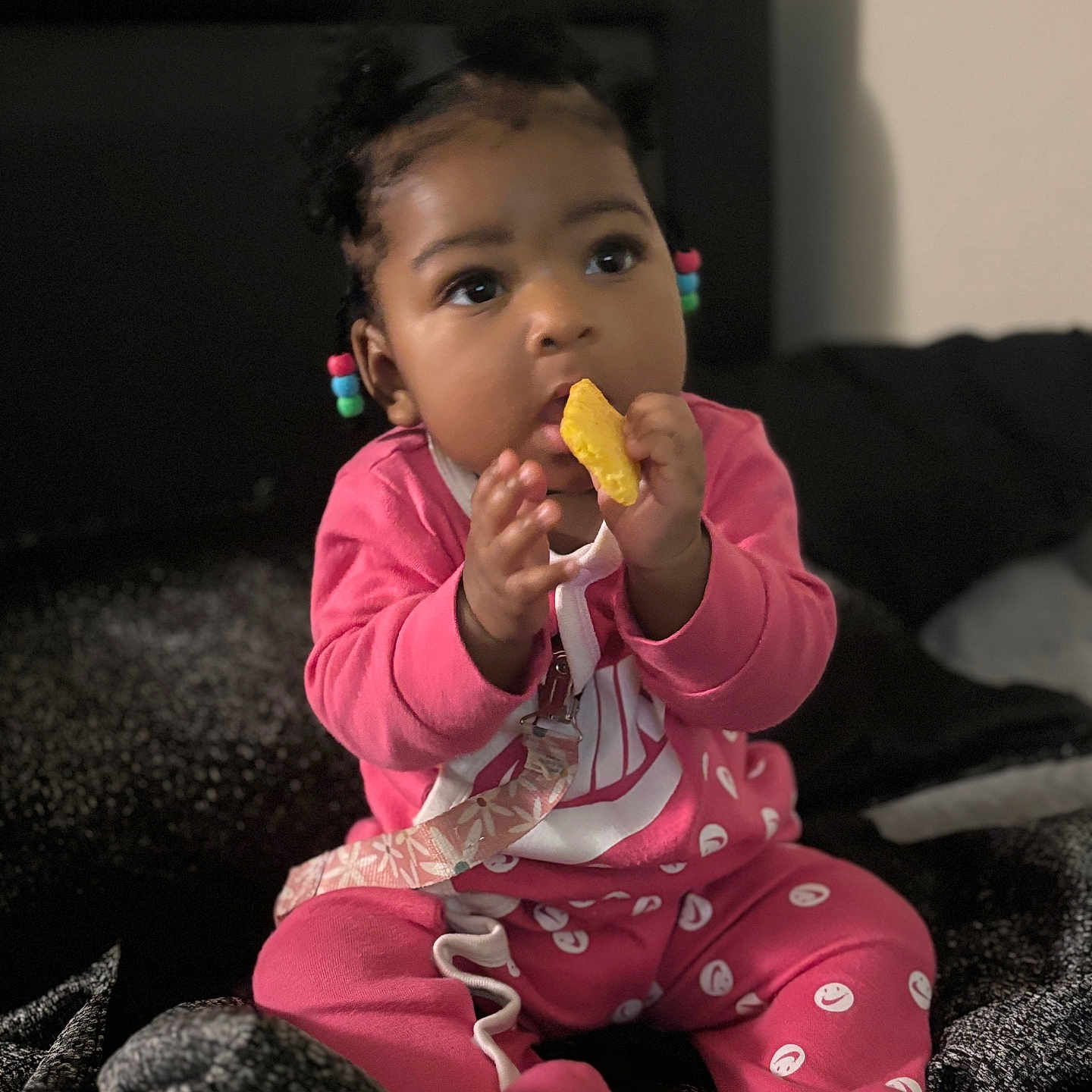 Kyzah joined the competition — help win amazing prizes! baby, bed, blanket, child, clothing, cozy, curious_expression, cute, face, hair_beads, hand_to_mouth, indoors, infant, person, pink_clothing, portrait, sitting, smiling_faces_pattern, snack, young_child