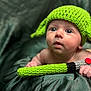 baby, infant, knitted_hat, green_hat, toy, knitted_toy, lightsaber, cute, child, portrait, soft_background, fabric, hand, blue_eyes, curious, young_child, indoor, closeup, face, expression