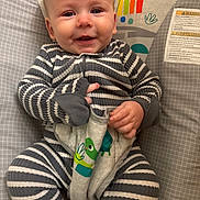 Sunnie is registered to the contest to win money with this photo: baby, infant, striped_onesie, smiling, baby_seat, toy, colorful, monkey_graphic, rainbow, cute, happy, child, indoor, portrait, comfort, soft_toy, hand, face, clothing, playful