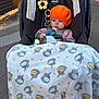 baby, infant, car_seat, blanket, toy, orange_hat, striped_clothing, outdoor, sidewalk, curious, child, face, seatbelt, warm_light, chicco, plush_blanket, small_toy, cute, sitting, wearing_hat