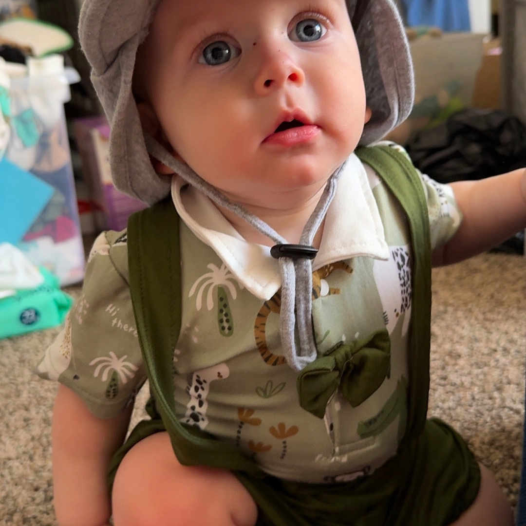 Sunnie joined the competition — help win amazing prizes! baby, blue_eyes, candid, carpet, casual, child, curious, cute, expression, face, footwear, green_clothing, hat, indoor, infant, person, portrait, sitting, suspenders, young_child