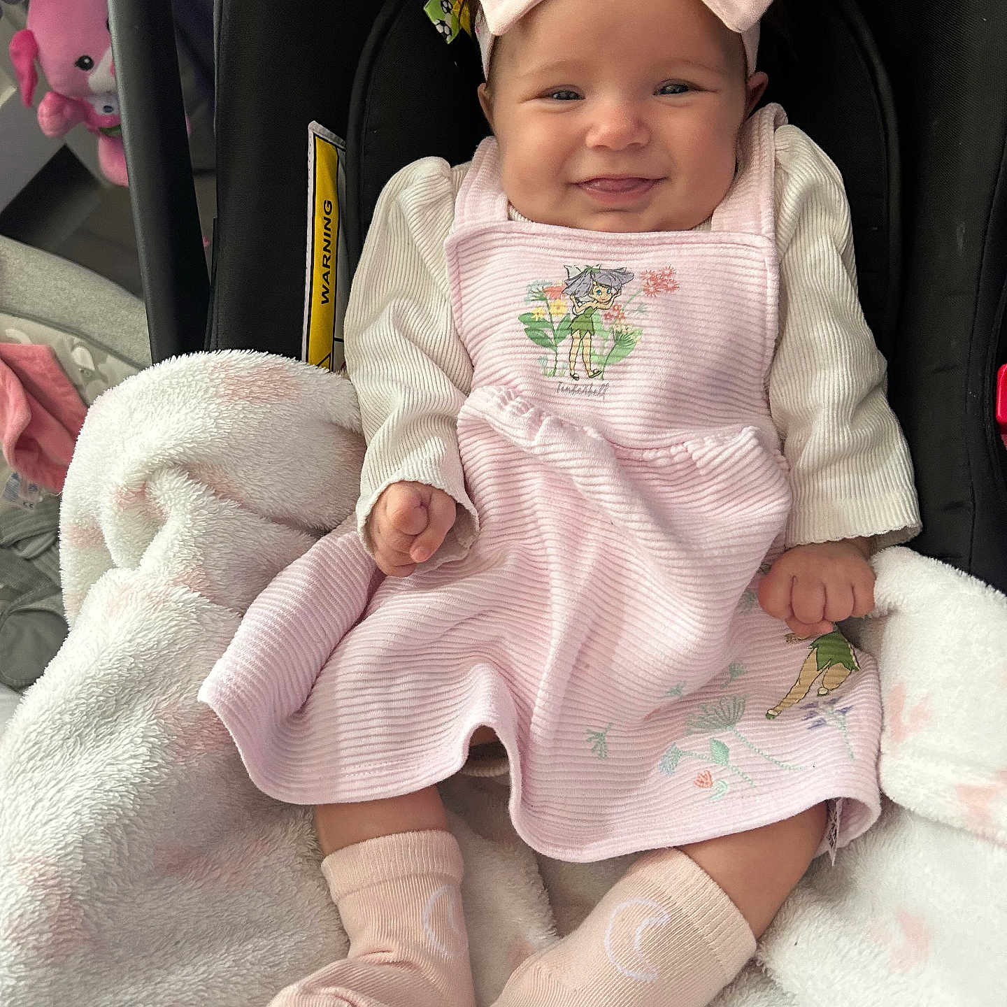 Maddie-Mae is registered to the contest to win money with this photo: baby, blanket, car_seat, child, clothing, cozy, cute, dress, happy, headband, indoors, infant, person, pink_bow, portrait, seated, smiling, socks, soft, toy