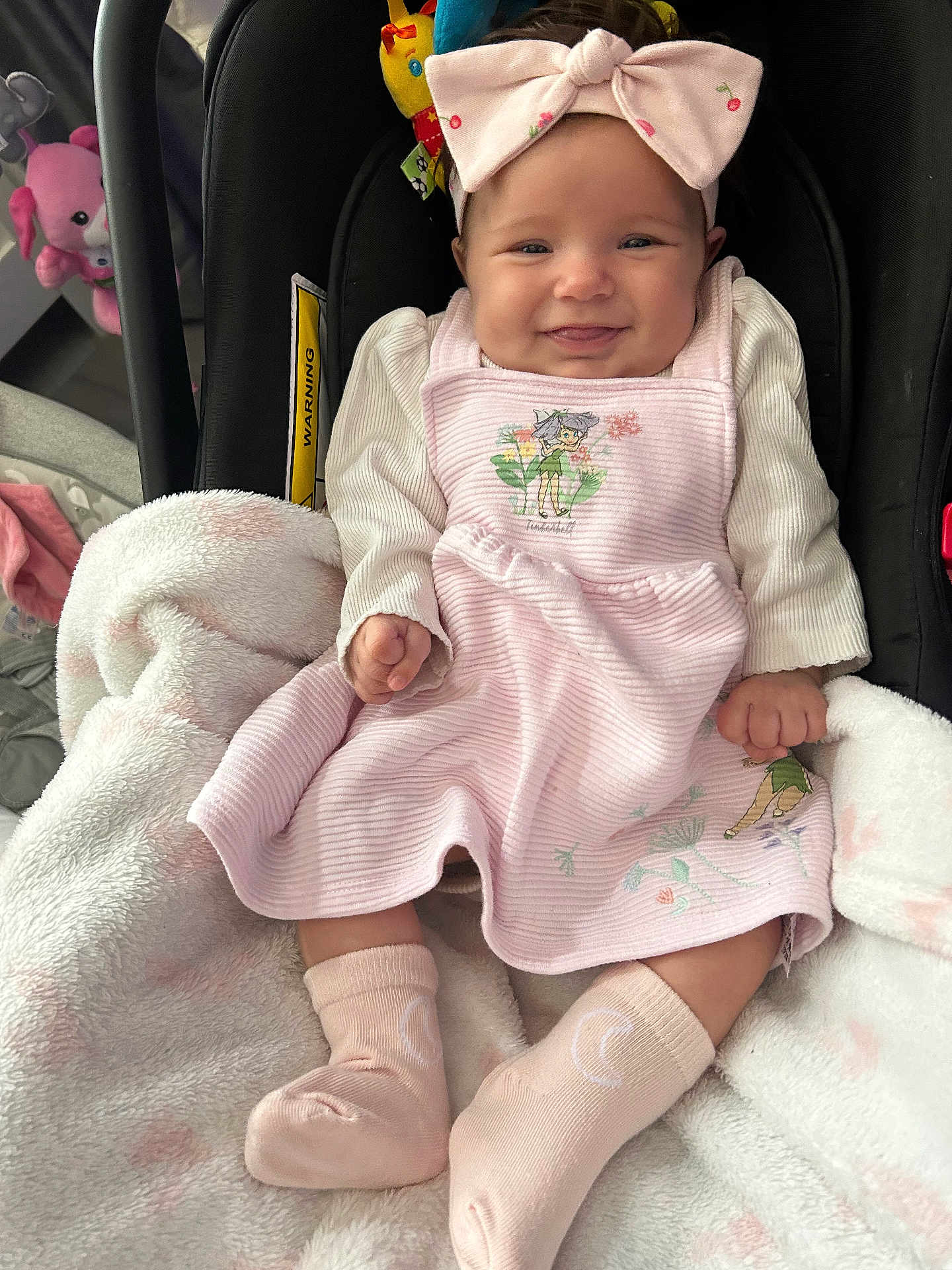 Maddie-Mae is registered to the contest to win money with this photo: baby, blanket, car_seat, child, clothing, cozy, cute, dress, happy, headband, indoors, infant, person, pink_bow, portrait, seated, smiling, socks, soft, toy