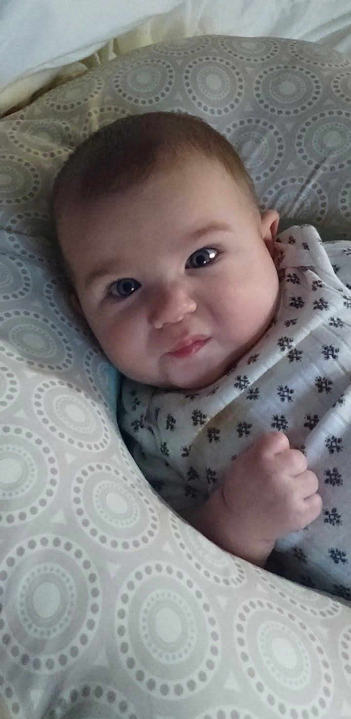 River is registered to the contest to win money with this photo: baby, infant, face, pillow, patterned_pillow, cute, expression, hand, fist, lying_down, bed, blanket, sleepwear, indoors, child, portrait, young, soft_lighting, closeup, resting