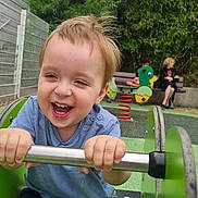 Gabriel a rejoint le concours — aidez-le/la à gagner de superbes lots ! child, toddler, playground, green, ride, smiling, happy, outdoor, bench, adult, toy, spring, grass, fence, nature, person, shorts, blue_shirt, daytime, fun