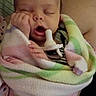 Ila is registered to the contest to win money with this photo: baby, newborn, sleeping, yawning, pacifier, blanket, swaddled, portrait, face, eyes_closed, indoors, bed, cozy, pastel, striped_blanket, infant, rubbing_eye, sitting, adult, home