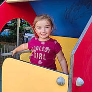 Cassandra a rejoint le concours — aidez-le/la à gagner de superbes lots ! child, girl, playground, play_structure, smiling, outdoor, tree, greenery, yellow_panel, red_panel, blue_panel, tshirt, short_sleeves, happy, person, daylight, park, cute, young, fun