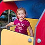 child, girl, playground, play_structure, smiling, outdoor, tree, greenery, yellow_panel, red_panel, blue_panel, tshirt, short_sleeves, happy, person, daylight, park, cute, young, fun