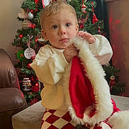 Lucas is registered to the contest to win money with this photo: celebration, child, christmas_tree, cozy_sweater, curious_expression, curtain, cute, decorations, festive_clothing, furniture, holiday, indoor, living_room, plush, red_and_white, santa_hat, seasonal, sitting, toddler, window