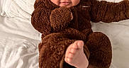 Raian is registered to the contest to win money with this photo: baby, child, fuzzy_clothing, brown_onesie, cute, smiling, foot, bed, white_bedspread, indoor, portrait, childhood, happy, playful, infant, cozy, warm_clothing, face, person, soft_texture