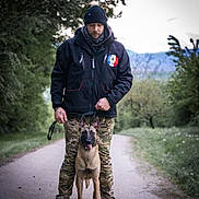 Urane participe au concours pour gagner de l'argent avec cette photo : beanie, black_jacket, camouflage_pants, canine, dog, forest, grass, happy_dog, leash, man, mountains, nature, obedient, outdoor, path, pet, portrait, scarf, trees, walking