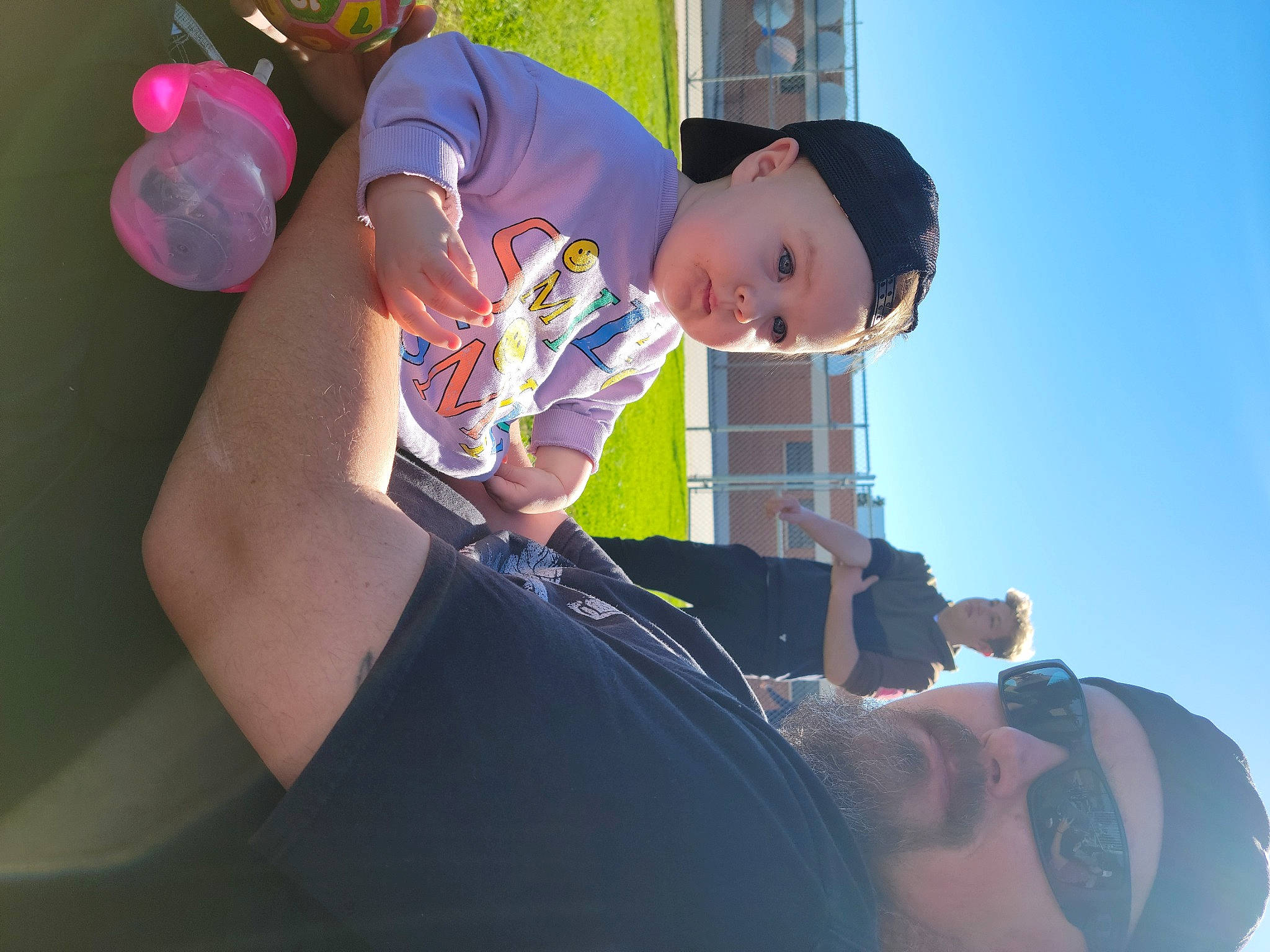 Ryan is registered to the contest to win money with this photo: arm, baby, balloon, child, elbow, eyewear, finger, fun, gesture, happy, hat, headwear, leisure, party_supply, person, personal_protective_equipment, recreation, sitting, sky, t_shirt