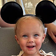 Maylin joined the competition — help win amazing prizes! adult, baby, beaded_necklace, blonde_hair, blue_eyes, bows, child, closeup, earrings, face, happy, headband, indoor, mickey_mouse_ears, portrait, sitting, smiling, toddler, vehicle, white_outfit