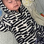 baby, sleeping, onesie, zebra_stripes, plush_toy, soft_texture, cozy, infant, child, cute, peaceful, face, closed_eyes, headwear, indoor, blanket, bed, pattern, young, resting