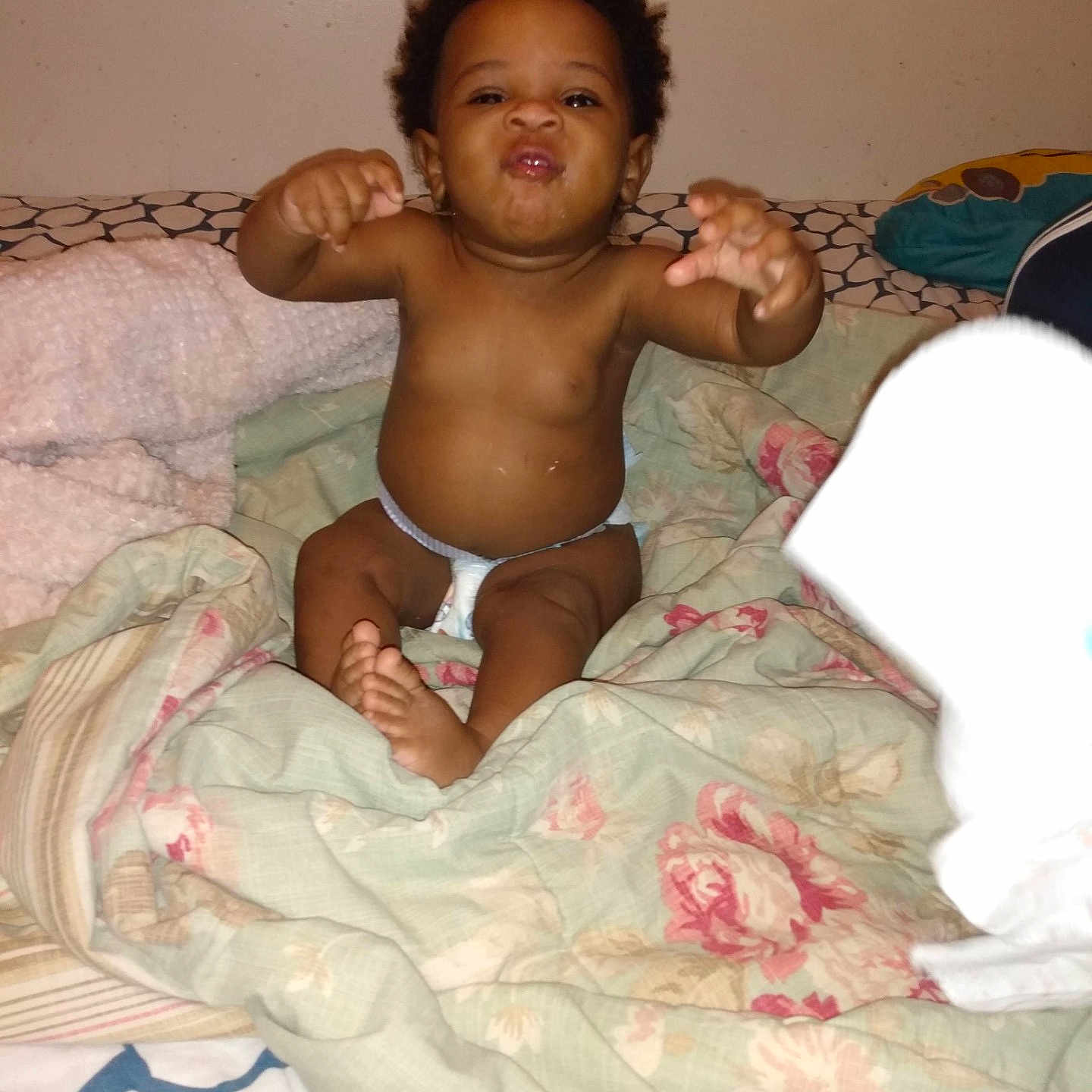 Pillow is registered to the contest to win money with this photo: arms, baby, bed, blanket, child, cute, diaper, expression, floral_pattern, furniture, head, indoor, infant, pacifier, patterned_blanket, person, playful, skin, smiling, wall