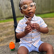 Kendall joined the competition — help win amazing prizes! toddler, child, glasses, chocolate, bunny, outdoor, toy, concrete, shorts, shirt, fence, grass, face, hands, sitting, expression, play, summer, daytime, portrait