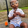 toddler, child, glasses, chocolate, bunny, outdoor, toy, concrete, shorts, shirt, fence, grass, face, hands, sitting, expression, play, summer, daytime, portrait