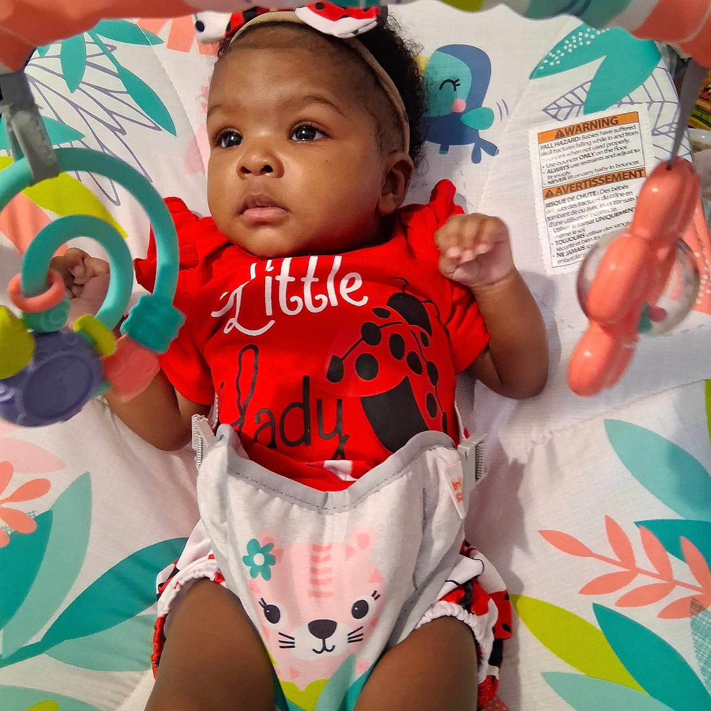 Phor'Ever is registered to the contest to win money with this photo: baby, infant, child, portrait, sitting, activity_center, toy, colorful, red_outfit, ladybug, bib, cat_bib, headband, smiling, wide_eyed, indoor, baby_seat, playtime, patterned_background, safe