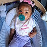 baby, child, infant, portrait, pacifier, pink_bows, hair_bows, smiling, rocker, baby_seat, striped_fabric, bib, floral, purple_clothing, indoor, nursery, blanket, seated, looking_at_camera, adorable