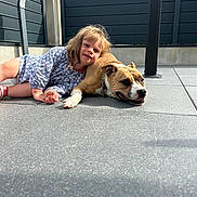 Jyna a rejoint le concours — aidez-le/la à gagner de superbes lots ! girl, child, dog, dog_face, pet, friendship, companionship, outdoor, patio, sunlight, portrait, lying_down, smiling, blonde_hair, dress, collar, chain, concrete, fence, family
