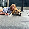 girl, child, dog, dog_face, pet, friendship, companionship, outdoor, patio, sunlight, portrait, lying_down, smiling, blonde_hair, dress, collar, chain, concrete, fence, family