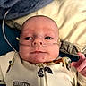 baby, bed, blanket, child, close_up, clothing, cozy, eyes_open, face, hand, hospital_tube, indoors, infant, lying_down, medical_equipment, nasal_cannula, newborn, onesie, pillow, portrait