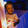 child, toddler, smiling, face, indoor, lighting, fairy_lights, night, blue_background, clothing, happy, portrait, cute, baby, person, dark, decor, fabric, hand, playful