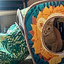 cat, orange_tabby, fabric_tunnel, lion_design, indoor, carpet, curious, peeking, pet, animal, playful, colorful, patterned, leaf_pattern, cozy, soft_lighting, feline, hiding, toy, home