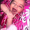 baby, black_border, blanket, child, close_up, cute, face, floral_pattern, hand, heart_doodle, indoor, infant, lying_down, patterned_clothing, phone_screenshot, pink, portrait, sleepy, smiling, yawning