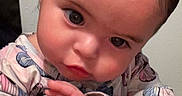 Amara Garcia is registered to the contest to win money with this photo: adult_hand, baby, butterfly, child, close_up, eyes, face, hands, held, indoor, infant, patterned_clothing, photograph, pink, portrait, serious, sitting, smartphone_screenshot, wall, white