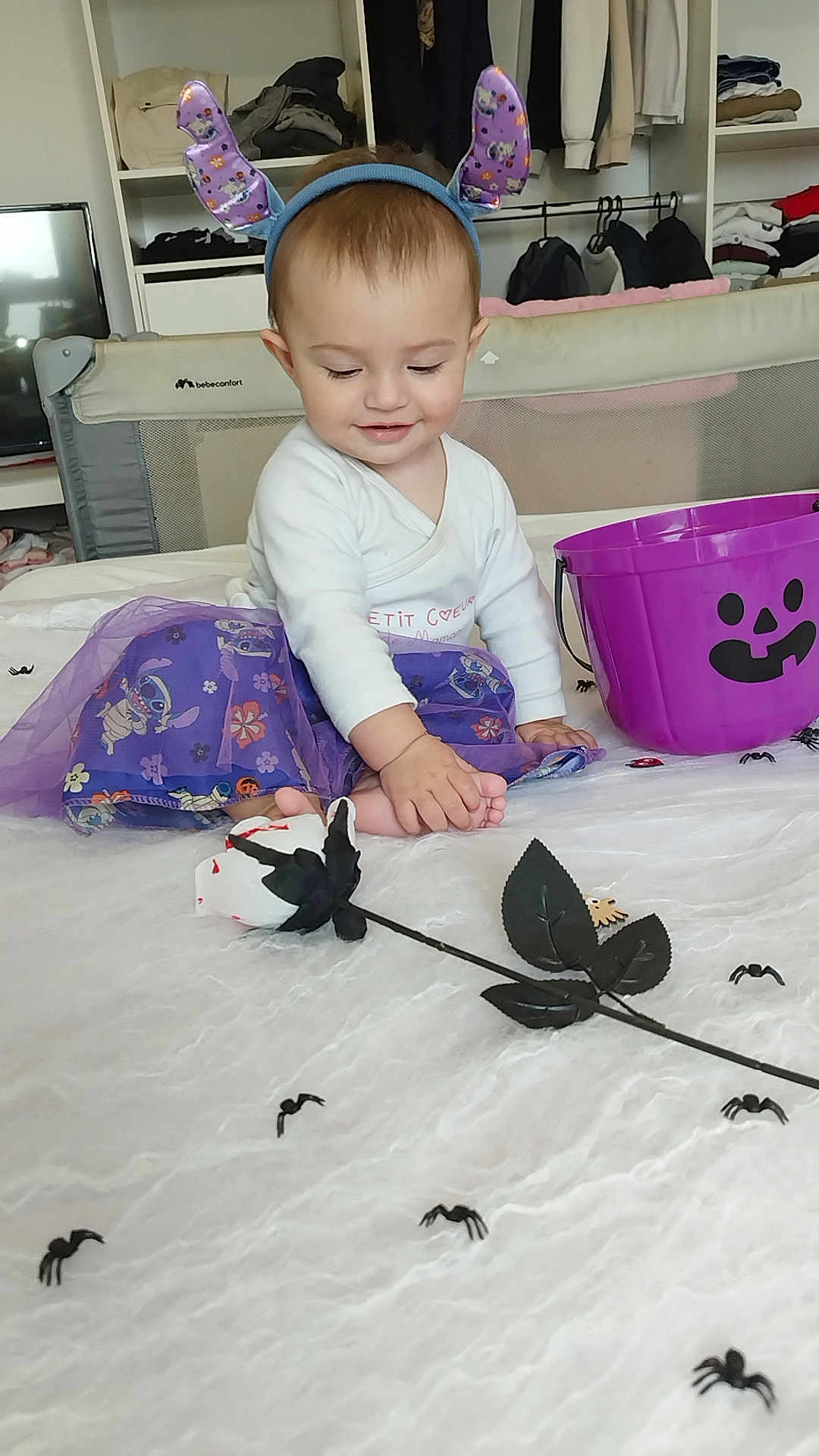 Juliana a rejoint le concours — aidez-le/la à gagner de superbes lots ! baby, child, purple_skirt, headband, ears, toy_spiders, halloween_bucket, bedspread, room, curious, sitting, foot, white_clothing, indoor, playful, decorations, toys, smiling, cute, costume