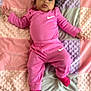 baby, child, pink_clothing, nike_logo, blanket, pastel_colors, curly_hair, socks, infant, lying_down, soft_texture, cute, portrait, indoors, comfort, toddler, face, person, sleepwear, resting