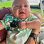 baby, child, person, infant, tie_dye_shirt, holding, arm, outdoor, grass, car, vehicle, watch, tattoo, face, expression, clothing, casual, skin, portrait, cute