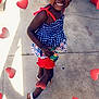 child, girl, smiling, posing, sidewalk, outdoor, red_shorts, blue_top, sandals, hairband, curly_hair, sunlight, heart_graphics, playful, happy, person, summer, casual_clothing, concrete, shadow