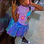 child, girl, posing, phone, peace_sign, tutu_skirt, cartoon_shirt, reflection, night, concrete_floor, black_shoes, braided_hair, casual_clothing, playful, outdoor, sidewalk, window, reflection_in_glass, colorful_outfit, young_person
