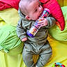 baby, infant, child, toy, rattle, colorful, green_clothing, cushion, soft_toys, playtime, cute, indoors, lying_down, sock, small_hands, head, face, chewing, bright_colors, relaxing