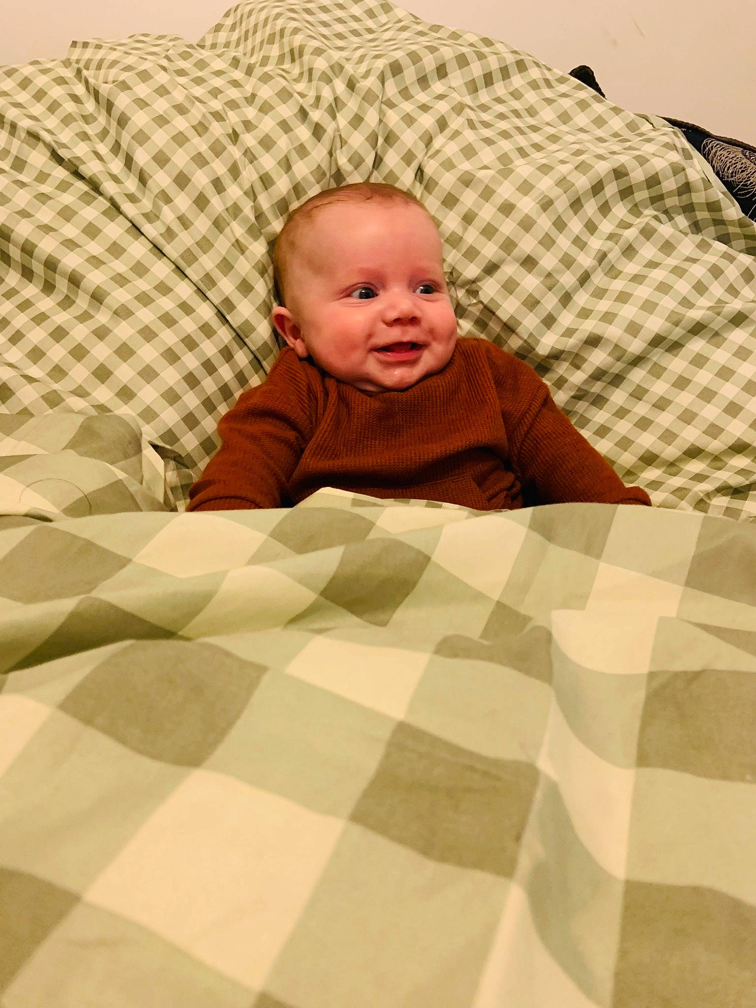 Toby is registered to the contest to win money with this photo: baby, baby_toddler_clothing, bed_sheet, bedding, child, comfort, crawling, floor, flooring, grass, hardwood, linens, pattern, person, product, room, sitting, smile, textile, toddler