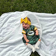 Luciella is registered to the contest to win money with this photo: baby, child, smiling, green_bay_packers, dress, yellow_bow, headband, white_blanket, grass, outdoor, happy, sitting, infant, cute, sock, white_sock, portrait, soft_texture, sportswear, baby_fashion