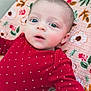 baby, infant, child, face, eyes, red_clothing, onesie, blanket, floral_pattern, cute, portrait, lying_down, skin, head, expression, small_heart_pattern, person, indoors, soft_light, young
